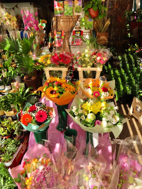 An array of fresh floral arrangements displayed on a pink table at Highbury Flowers, showcasing vibrant bouquets wrapped in colorful paper and placed in green and white vases. The bouquets feature a v