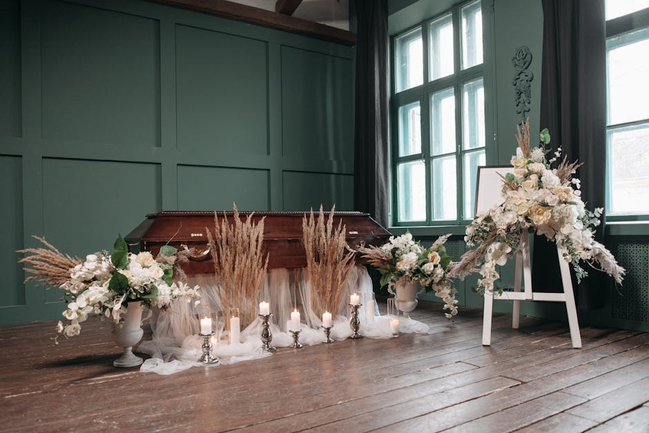 A floral arrangement featuring large white roses, orchids, and soft pink and cream flowers, complemented by beige pampas grass and green foliage, all arranged in elegant vases on either side of a wood