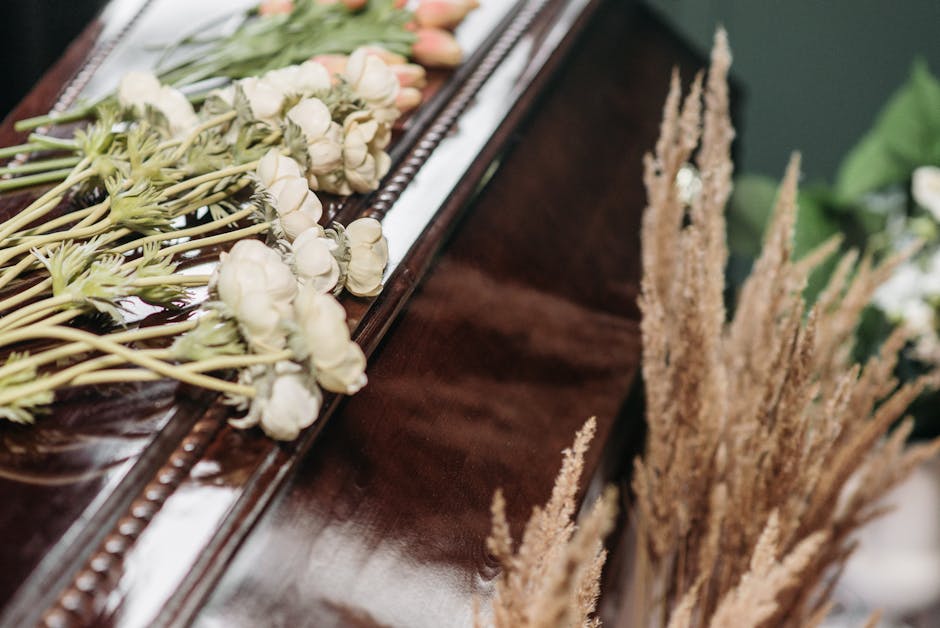 A close-up view of an elegant floral arrangement on a polished wooden surface, featuring a variety of flowers in soft, neutral tones. The bouquet includes cream and pale peach roses with layered petal
